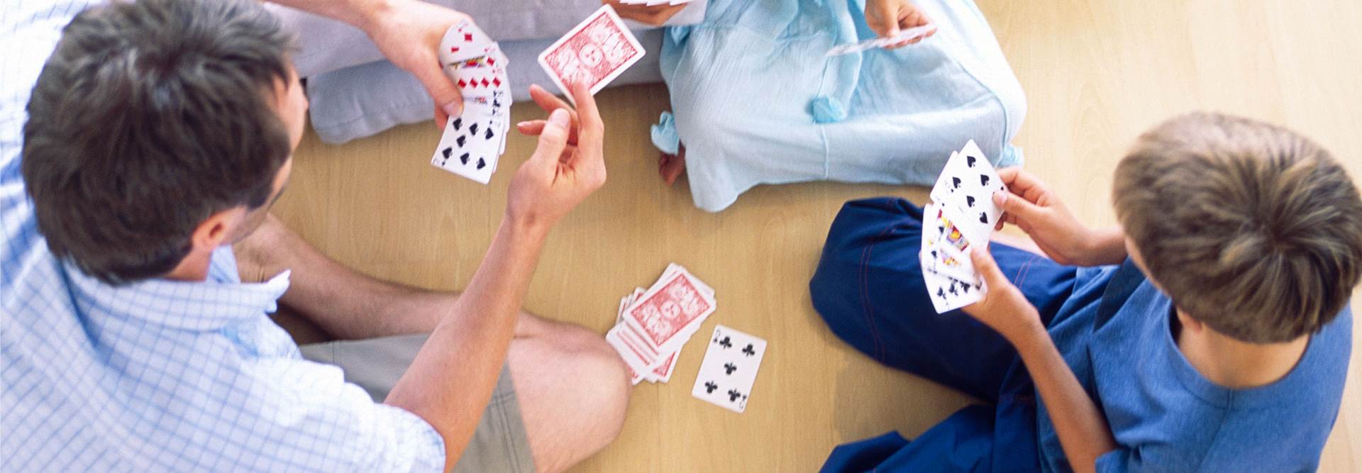 Mãe, pai e 2 filhos jogam as cartas no chão da sua casa.