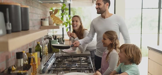 Mae, pai e dois filhos cozinham em conjunto num fogão a gás