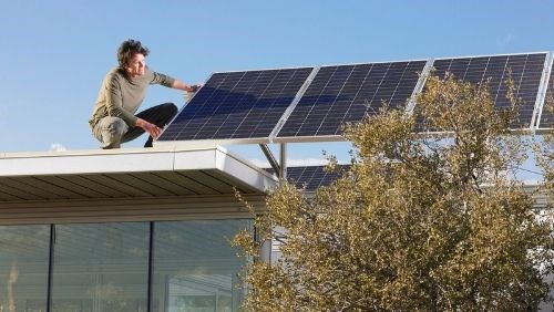 Homem a instalar paineis solares no topo da casa