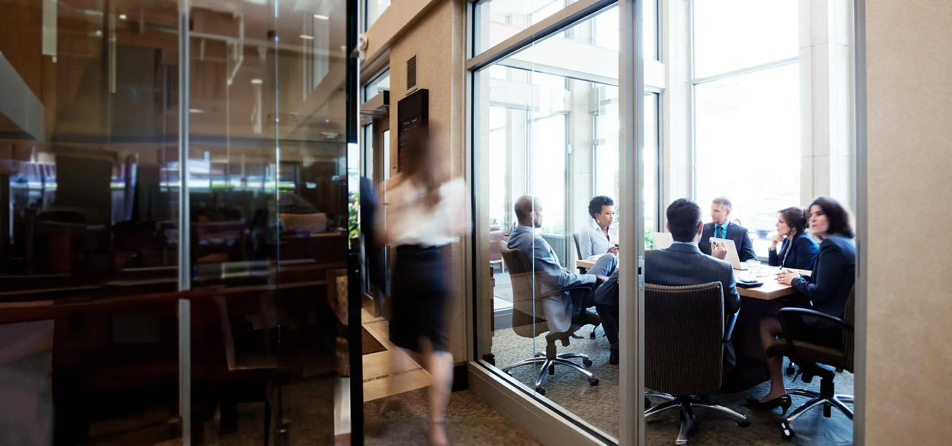 Sala de reuniões vista através de um vidro com 3 homens e 3 mulheres em reunião