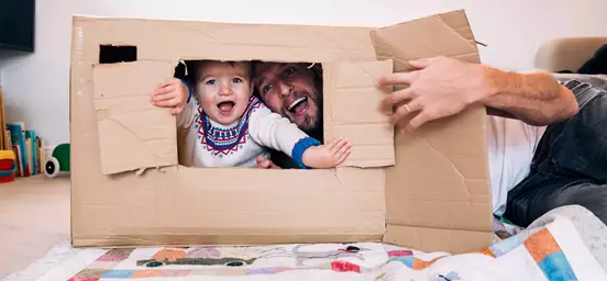 Pai e filho a brincar espreitam por uma caixa de papel