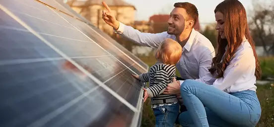 Pai, mãe e bébe na relva a tocarem num painel solar