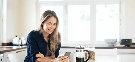 Mulher com telemóvel numa bancada ao lado de café e cereais 