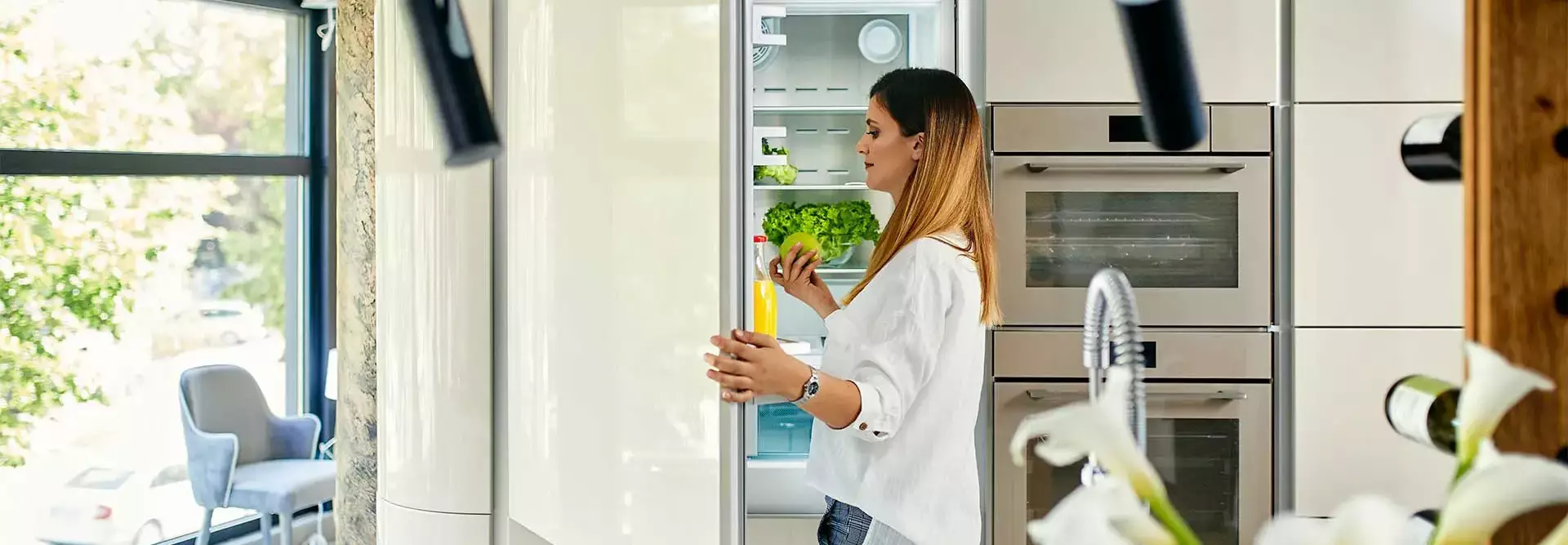 Mulher na cozinha abre o frigorifico para tirar uma maçã